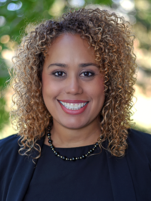 A person with curly, shoulder-length hair and a broad smile.