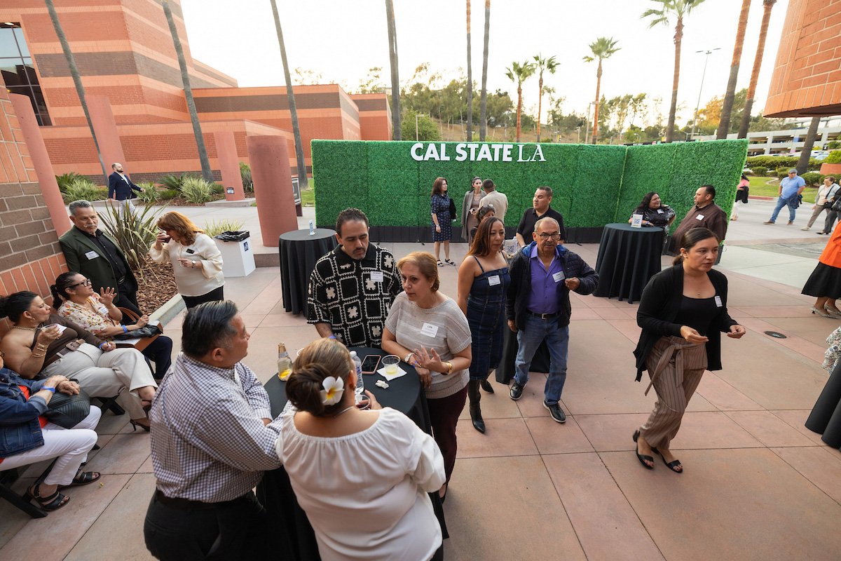 Group of people milling around in front of green hedges with a sign that says Cal State L.A.