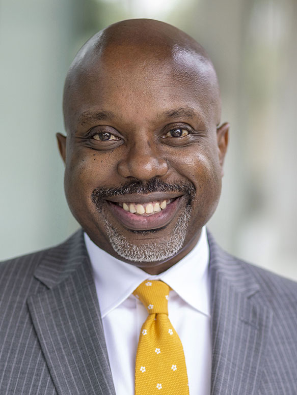 A person wearing a suit and tie smiling.