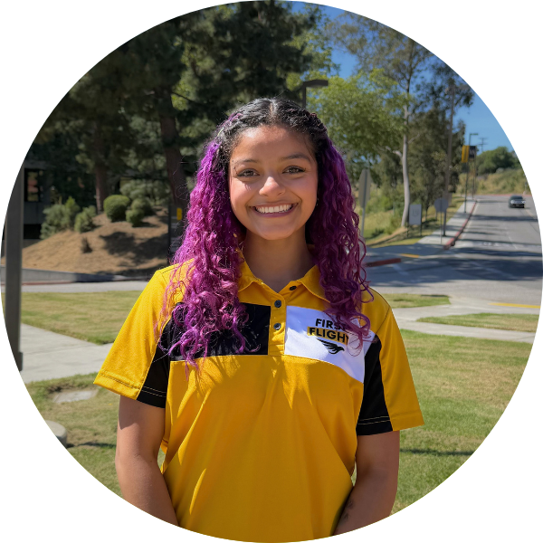 A woman with purple hair and a yellow polo smiling.