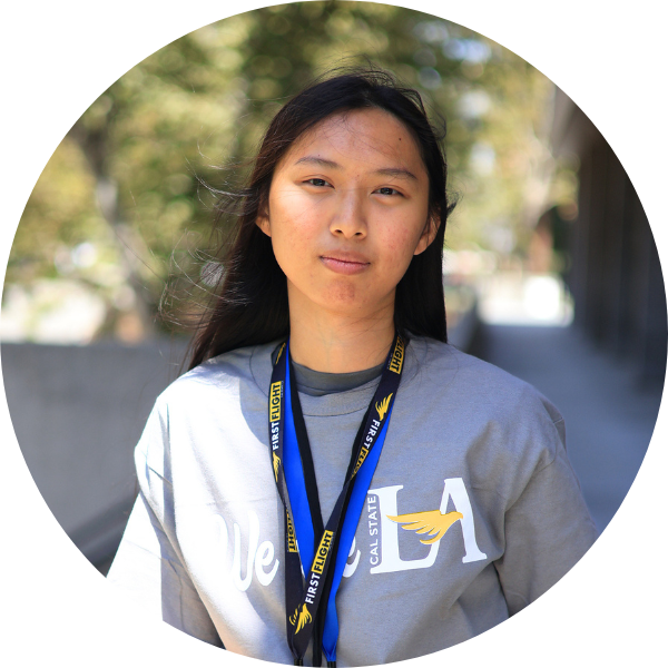 A woman with a grey shirt and black / blue lanyard facing the camera.