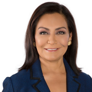 Headshot of woman with blue blazer and dark hair with gold earrings