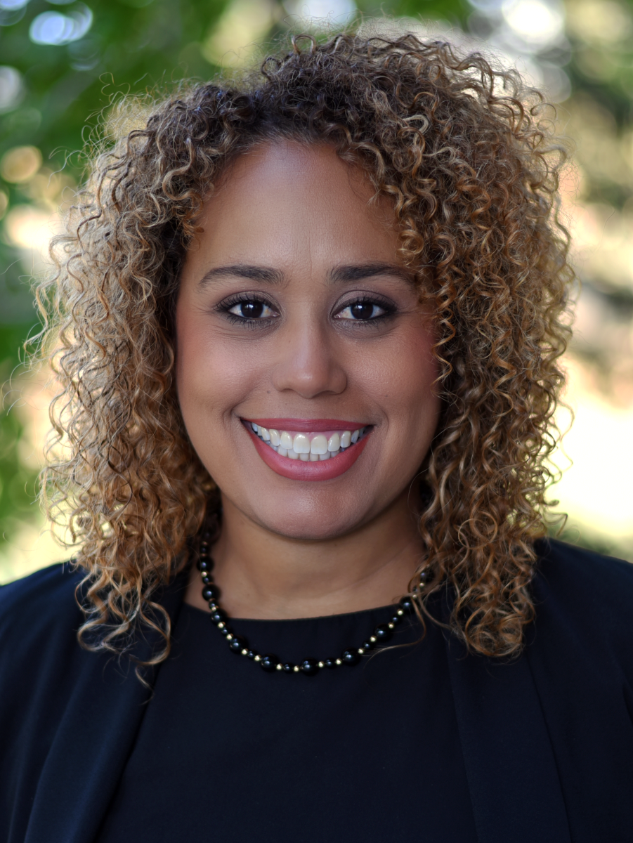 A person with shoulder-length curly hair smiling.