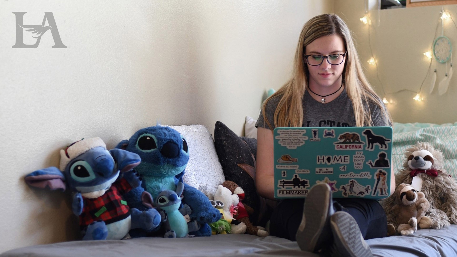 A student types on their laptop while sitting on their bed.