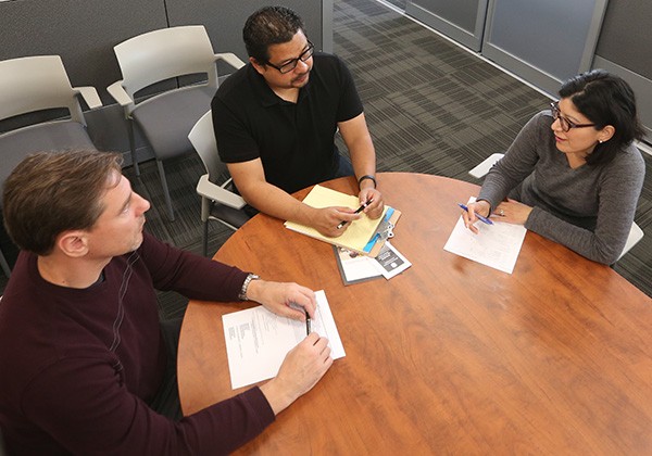 3 people sitting around table, evaluating paperwork