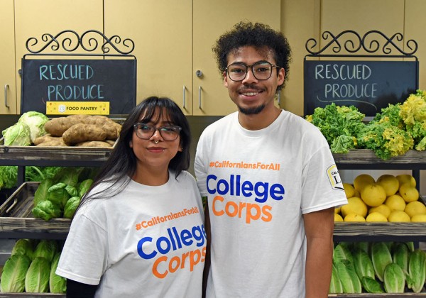 Two students wearing matching College Corps t-shirts while standing inside a Food Pantry.