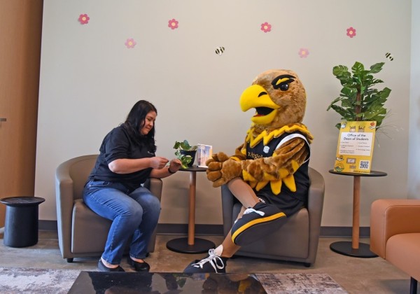 Female employee sitting on a couch next to Eddie the Golden Eagle Mascot