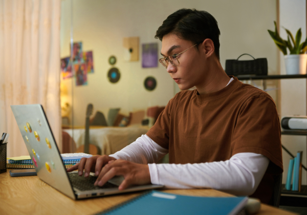 Student at home at desktop looking at laptop.