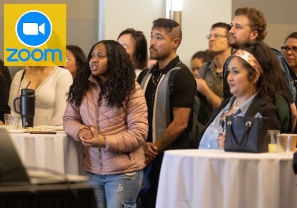 A group of conference attendees stands around high-top tables, attentively watching a presentation during an event. A Zoom logo appears in the upper-left corner, indicating the session is available virtually or via livestream.