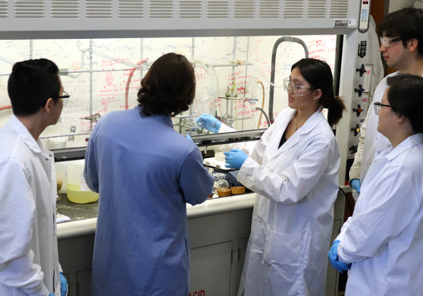 Dr Yangyan Lin with students in lab coats working an equation on glass in lab