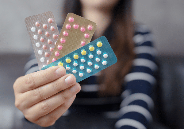 Woman in faded in background holding birth control pill packets in foreground