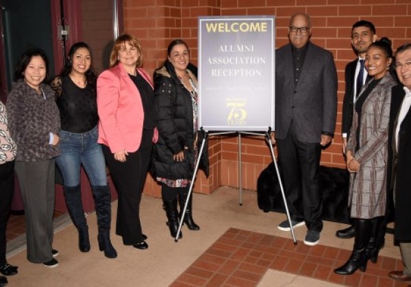 Nine alumni volunteers smiling and posing next to a poster that reads "Welcone alumni association reception March 24, 2023"