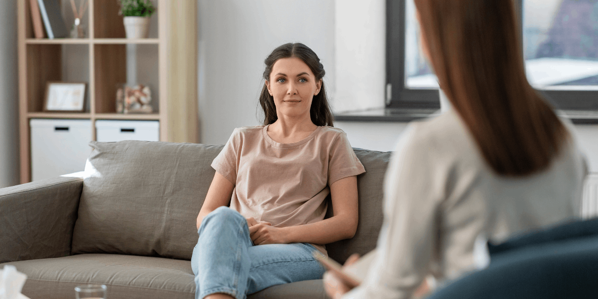 Women sits on sofa. Another woman sits across from her.