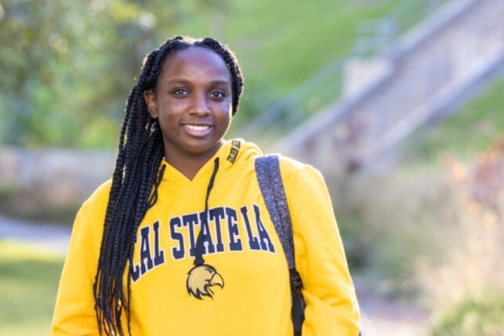 Student wearing yellow hoodie smiling with a backpack on.