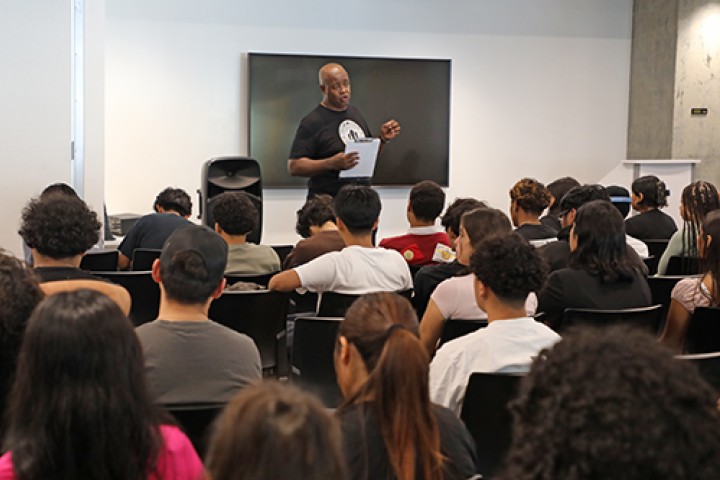 A staff member stands speaking to a room full of students.