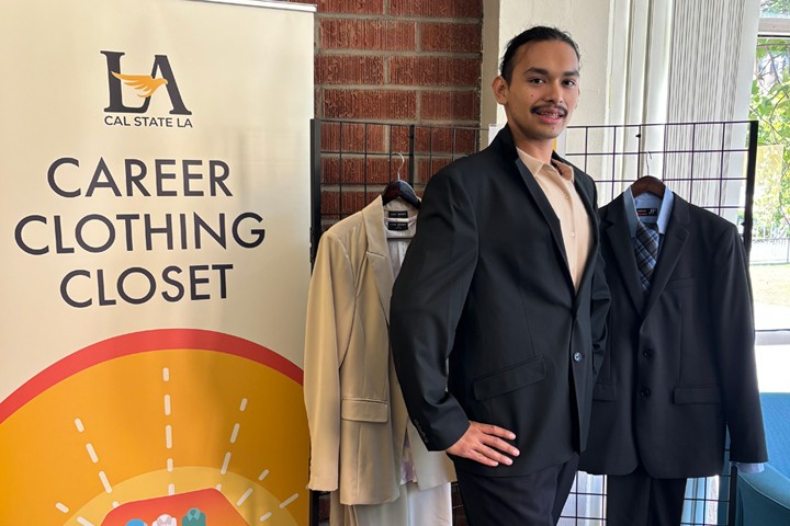 Student confidently wears professional suit and shoes in front of Career Clothing Closet display.