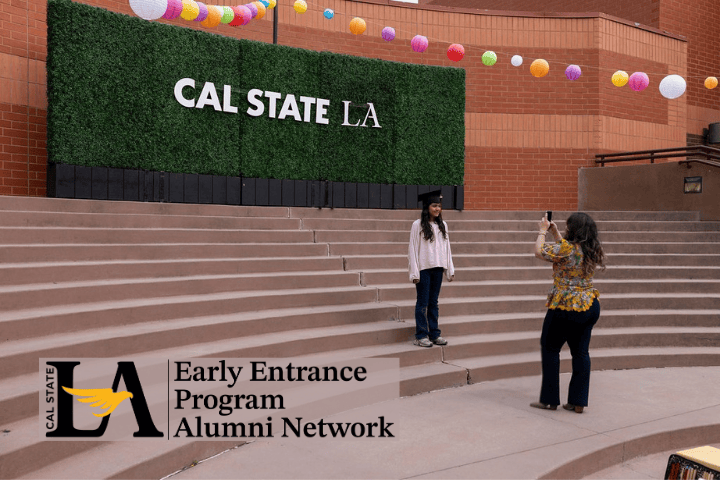 Youth wearing a graduation cap posing in front of a hedge with a Cal State LA sign as onlooker takes their photo