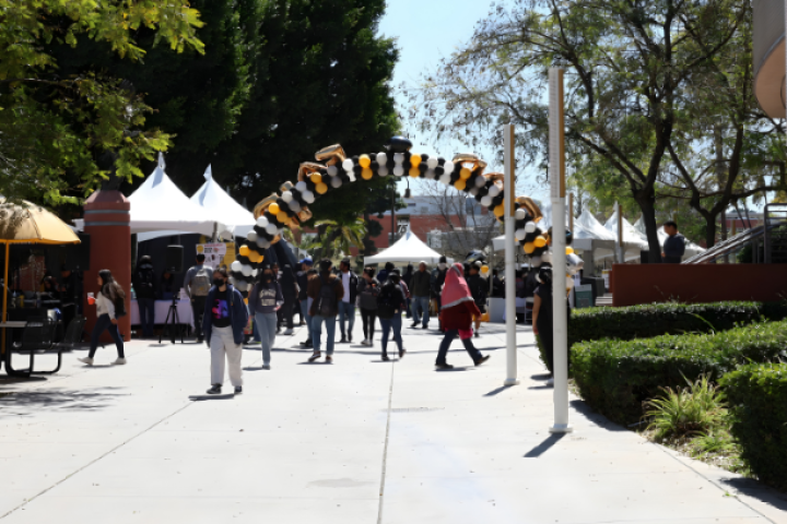 Students walk along Grad Fair, passing under a black, white, and gold balloon arch.
