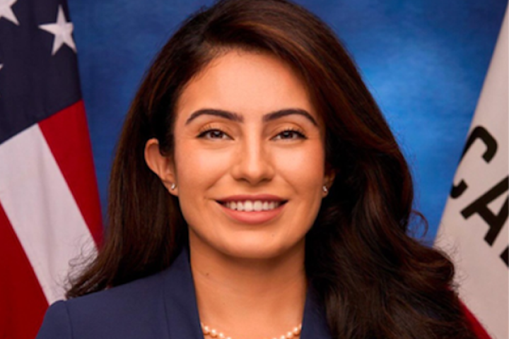 Senator Sasha Renée Pérez wearing a blue blazer standing in front of a United States and California Flag