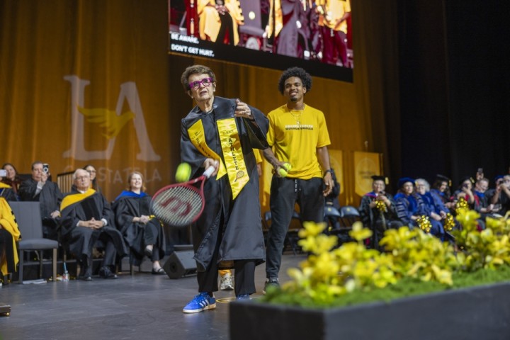 Billie Jean King hits a tennis ball with a racquet on stage.