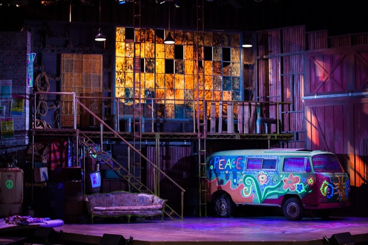 A wide shot of a past production of Hair, complete with Volkswagen bus onstage.