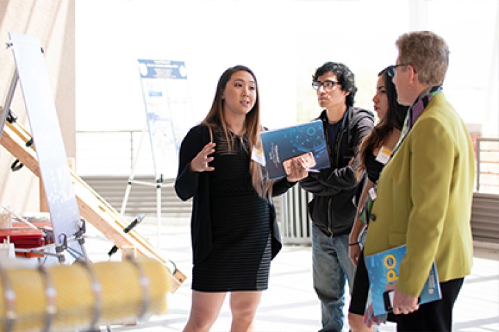 Female student professionally presenting to peers and Dean/faculty