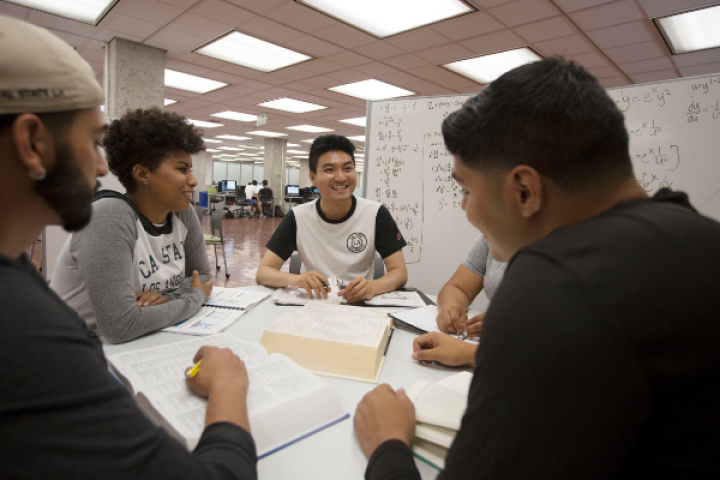 four students (three males and one female) sitting around a white table and writing apparati