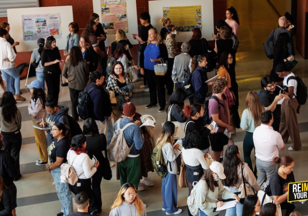 A busy event with people standing and reviewing poster presentations in an open indoor space