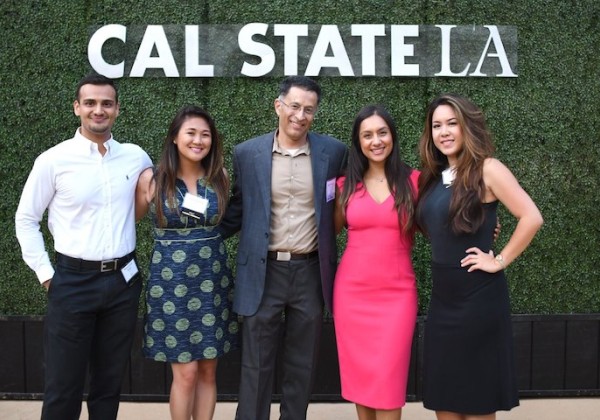 Five smiling alumni posing in front of Cal State LA banner