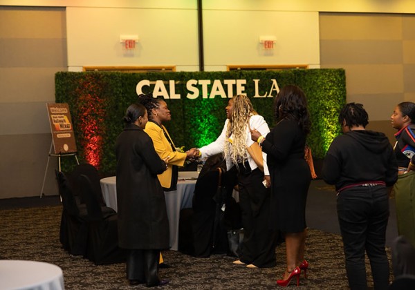 A group of people standing in front of a backdrop and two are shaking hands.