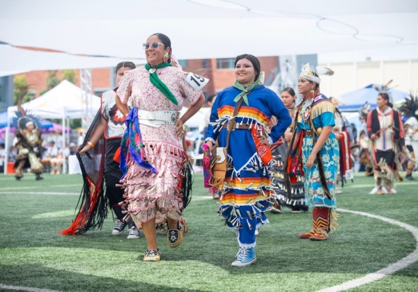 Participants wearing colorful regalia walk across the field during the grand entry at the Cal State LA Pow Wow.