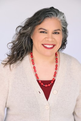 A photo of Dr. Linda Margarita Greenberg, a Latina woman in a cream sweater with a red necklace.