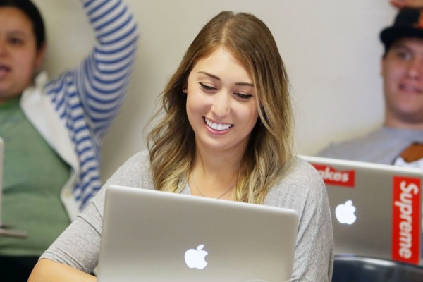 Image of a Caucasian female student smiling in a classroom setting in front of an open laptop. 