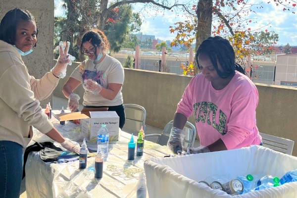 Three students smiling and creating a tie-dye shirt.