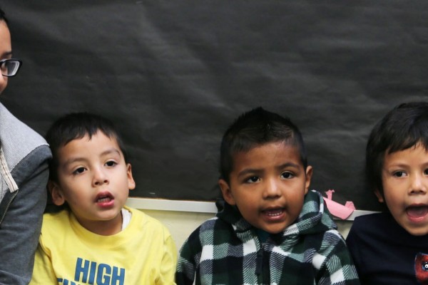 Image of a Cal State LA female student sitting next to three small children who appear to be singing. 