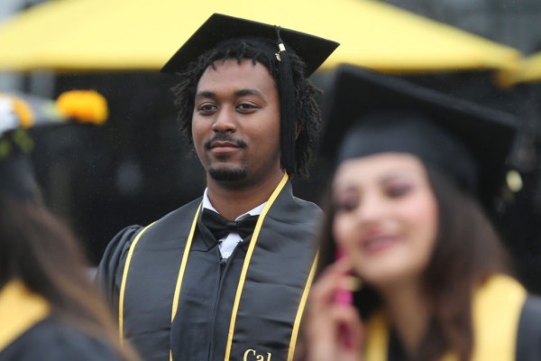 Image of a Black male student in Commencement regalia with a stoic expression on his face. 