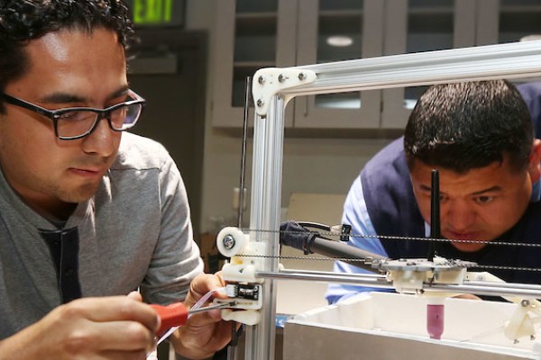 Image of two engineering students looking at a metal frame device intently. 