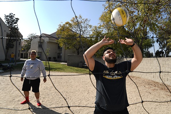 View through a volleyball net of a person about to make contact with a volleyball.