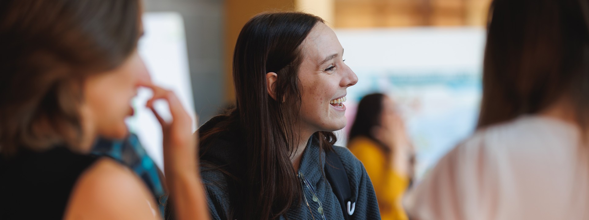 A young woman smiles while engaging in a conversation at the event, with people in the background.