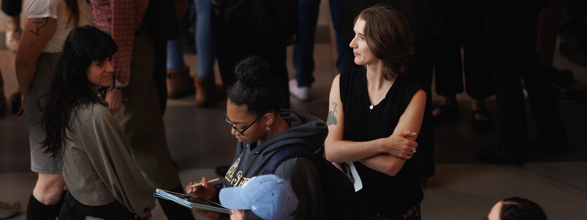 A diverse group of attendees gather, some taking notes and others engaged in conversation, in a large indoor event space.