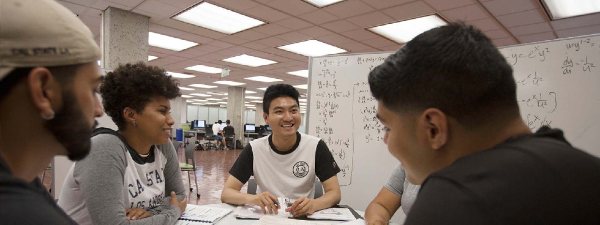 Group of students gathered in the library around a dry-erase board, studying. 